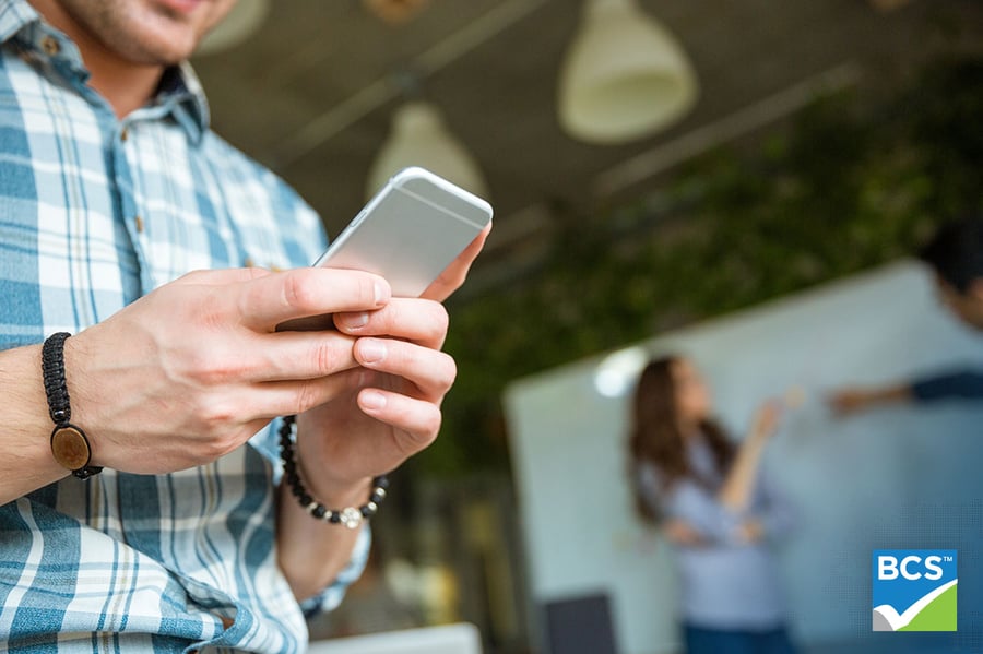 Closeup of hands of young man in checkered shirt using mobile phone 