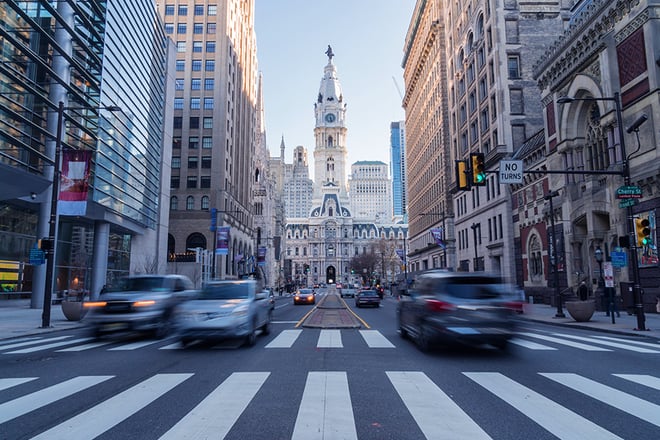 Downtown Philadelphia with City Hall in the background with cars moving quickly in the foreground.