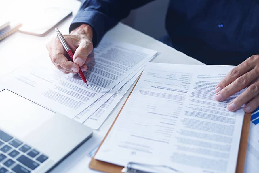 Closeup of a person reviewing and signing insurance documents at their desk in front of a laptop.